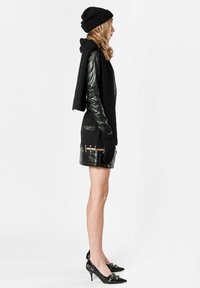 Gorro negro y bufanda de punto combinados con una chaqueta ajustada de cuero negro, minifalda de talle alto con detalles brillantes y tacones puntiagudos.