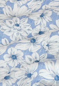 Biele kvety s modrými stredmi a jemnými tmavomodrými detailmi na textúrovanom svetlomodrom látkovom pozadí.