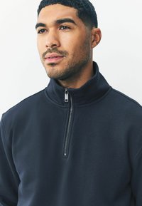Donkerblauwe fleecetrui met rits, voorzien van een hoge kraag, een gladde textuur en een zilveren ritsdetails. Minimalistisch ontwerp zonder patronen.