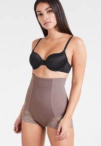 Reggiseno imbottito nero abbinato a pantaloni shorts modellanti marroni a vita alta con una parte frontale texturizzata e rifiniture in pizzo sui lati.