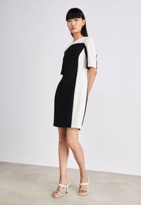 Schwarz-weißer Farbkantenkleid mit kurzen Ärmeln, Bootsausschnitt und geradem Schnitt. Getragen mit beigen High-Heels.