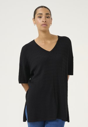 Top tricot noir avec un col en V, des manches courtes, un motif texturé et des fentes latérales, associé à un jean bleu. Finition en tissu lisse.