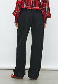 Jeans neri a gamba larga con vita alta, dotati di tasche posteriori e risvolti. Indossati con un top a quadri rosso e sandali rossi.