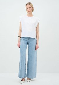 Vit ärmlös topp med texturerade detaljer, kombinerad med högmidjade ljusblå vida jeans och spetsiga vita klackar.