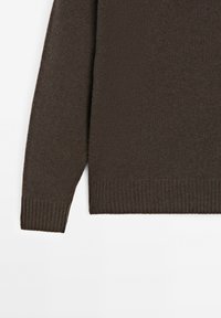 Dunkelbrauner gestrickter Pulloverärmel und unterer Torso mit gerippten Bündchen und Saum auf einem weißen Hintergrund.