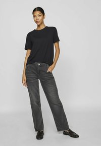 Must mustaga, vabalt istuv, koos kulunud hallide sirgete jalgade teksadega. Teksadel on toorikäär, kui need on stiilsed mustade kingadega.