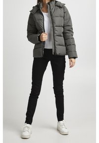 Szara pikowana kurtka z zamkiem błyskawicznym z przodu, z przymocowanym kapturem i prążkowanymi ściągaczami; w zestawie z czarnymi obcisłymi spodniami i białymi trampkami.