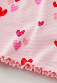 Tessuto rosa a coste con motivi di cuori rossi, rosa e rosa chiaro e un bordo arricciato nella parte inferiore.