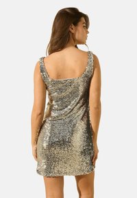 Robe mini en sequins argentés avec un décolleté carré et des bretelles fines, présentant une silouhette ajustée et un éclat texturé.