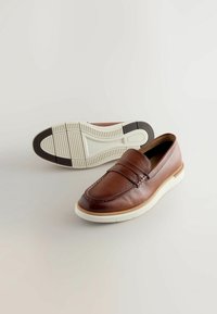 Mocassins en cuir marron avec un motif cousu, une couture surélevée et une semelle en caoutchouc blanche. La semelle présente un motif texturé pour une meilleure adhérence.