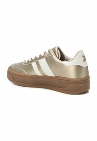 Zapatilla metálica dorada con franjas blancas, suela de goma, cuello acolchado y textura suave. Presenta un logo en el talón.