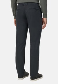 Pánske tmavosivé nohavice s rovnomerným strihom, s vystuženými zadnými vreckami na zips a hladkým, ľahkým materiálom. Nosia sa s čiernymi teniskami.