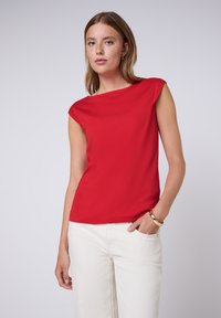 Haut rouge à manches courtes avec un décolleté bateau, fabriqué en tissu lisse. Assorti à un pantalon blanc à jambes larges, avec un design épuré.