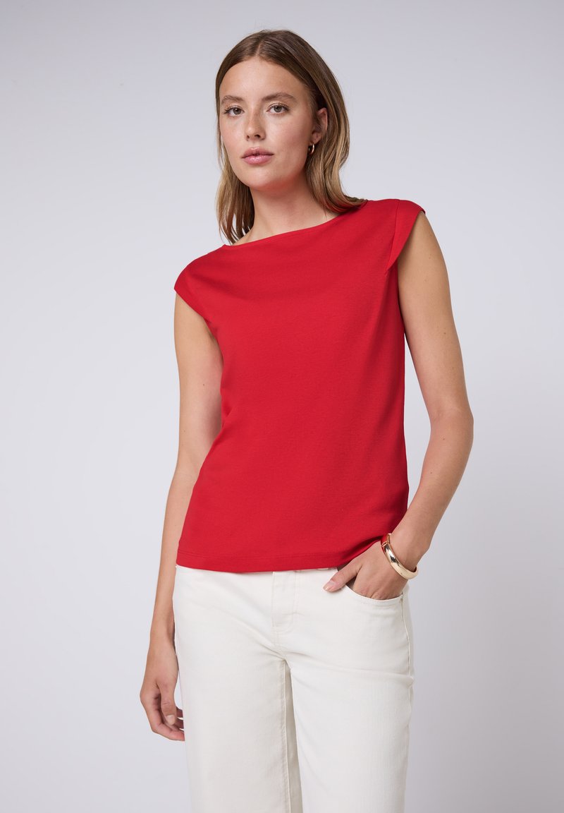 Haut rouge à manches courtes avec un décolleté bateau, fabriqué en tissu lisse. Assorti à un pantalon blanc à jambes larges, avec un design épuré.