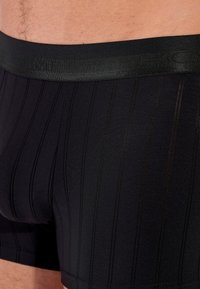 Mustat bokserit, joissa on tyylikäs muotoilu, kiiltävä vyötäröosa ja hienovaraiset pystysuorat raidat pehmeässä, venyvässä kankaassa.