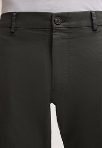 Dunkelgrüne Hosen mit Reißverschluss und Knopfverschluss, Fronttaschen und einem glatten, leichten Stoff. 