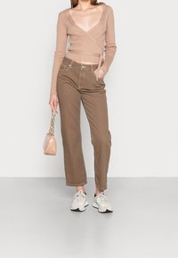 Beige ribbed wrap sweater, high-waisted brown wide-leg pants, light sneakers, and a small textured handbag with chain strap.