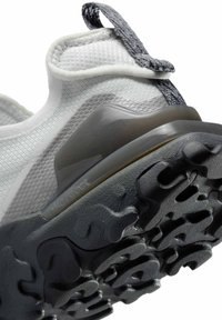 Witte sportieve schoen met een gestructureerde stoffen bovenkant, rubberen zool met een golfpatroon en een grijze trekband aan de hiel.