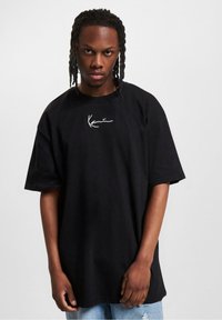 Black cotton oversized t-shirt featuring a white embroidered logo on the chest. Short sleeves and relaxed fit enhance comfort.