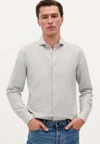 Lysegrå skjorte med knap-up lavet af blødt stof. Har en klassisk krave, lange ærmer og et lille logo på brystet. Bæres med blå jeans.