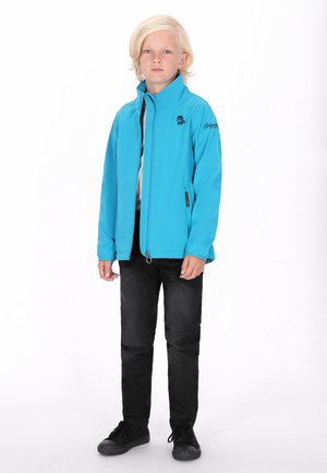 Blå softshell-jakke med høj krave, lynlåslukning foran, sorte detaljer, båret over en grå skjorte, kombineret med sorte bukser og sko.