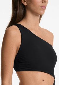 Crni top s jednim ramenom s glatkom teksturom, prilagođenim krojem i naborima sa strane, pogodnim za razne svakodnevne prigode.