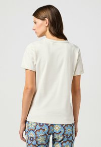 Camiseta de algodón color crema con escote redondo y mangas cortas, combinada con pantalones de patrón floral azul. Textura suave, ajuste casual.