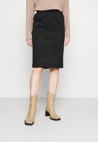 Hame black dengan tekstur halus dan pinggang elastis, dilengkapi dengan dua kantong depan. Dipadukan dengan sepatu bot pergelangan kaki berwarna beige dan atasan lengan panjang.