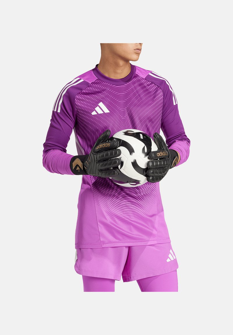 Lila Torwarttrikot mit Farbverlauf-Design, passende Shorts und schwarze Handschuhe, die einen schwarz-weißen Fußball halten. adidas-Branding sichtbar.