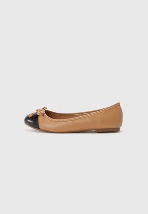 Chaussure de ballet plate beige pour femme avec un embout arrondi noir et un petit nœud à l'avant, présentée sur un fond clair uni.