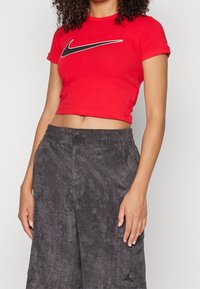 Czerwony krótki t-shirt z czarnym logo Nike w kształcie łyżwy, w połączeniu z ciemnoszarymi teksturowanymi spodniami cargo z kieszeniami i haftowanym logo.