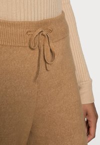 Beige breipantalons met een geribde tailleband en striksluiting, met een zachte textuur en subtiele glans, gecombineerd met een geribde top.