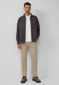 Geruite overhemd in navy en rood, witte t-shirt eronder, beige corduroy broek en bruine laarzen. Eenvoudig ontwerp zonder noemenswaardige accenten.