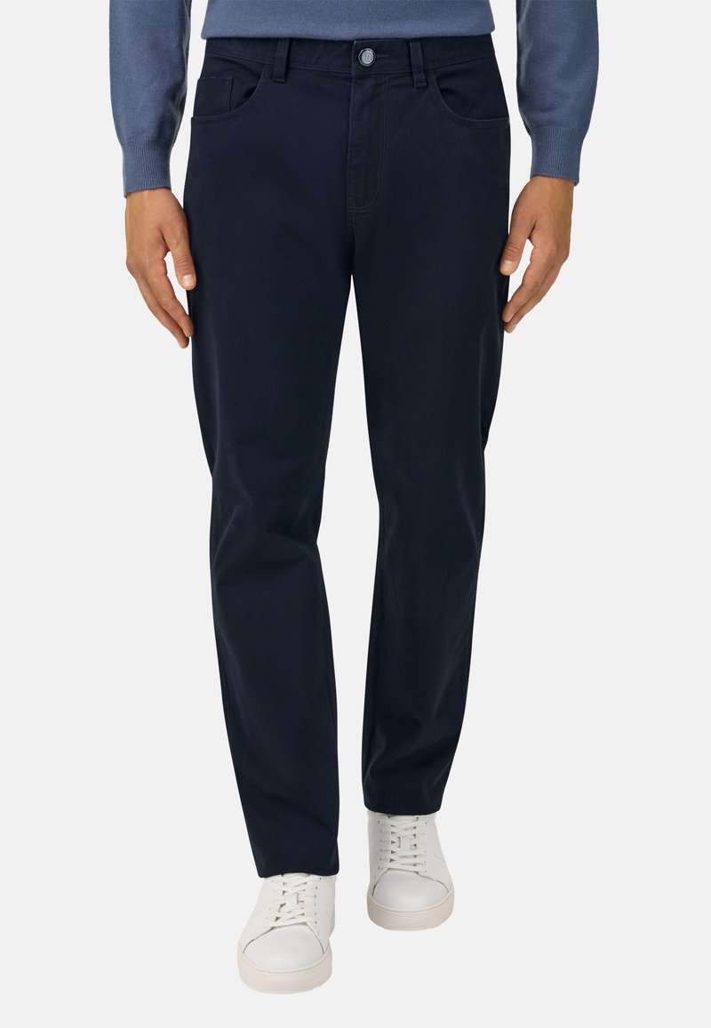 Tumed sinine puuvillane püksid sirge lõikega, millel on kaks esitaskut ja diskreetsed õmblused, koos valgete spordijalatsitega.