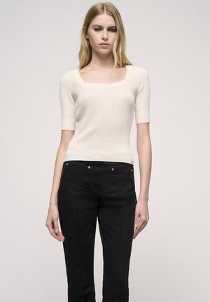 Crème korte mouwen trui met een textuur gebreide patroon en een vierkante halslijn, gecombineerd met slim-fit zwarte broeken met gouden accenten.