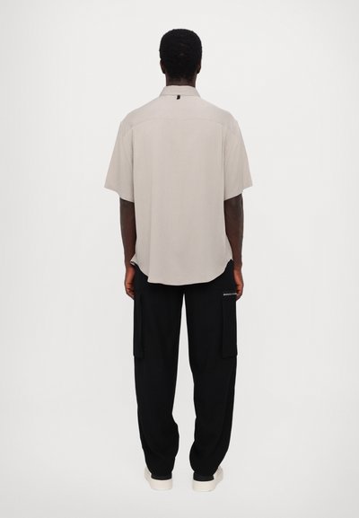 Chemise grise clair à manches courtes avec col, coupe droite et détail d'étiquette à l'arrière, associée à un pantalon cargo noir avec poches latérales.