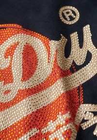 Marinfärgad tyg med ett metalliskt guld, orange och röd grafisk design, prydd med små, glänsande nitar i ett virvlande mönster.