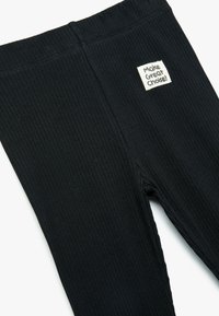 Svart ribbmönstrade leggings i stretchigt material, med en elastisk midja och en etikett som säger "Gör ett bra val."