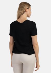 Top negru cu mânecă scurtă și decolteu rotund, dintr-un material moale, cu spate drapat și croială lejeră. Asortat cu pantaloni ajustați de culoare deschisă.