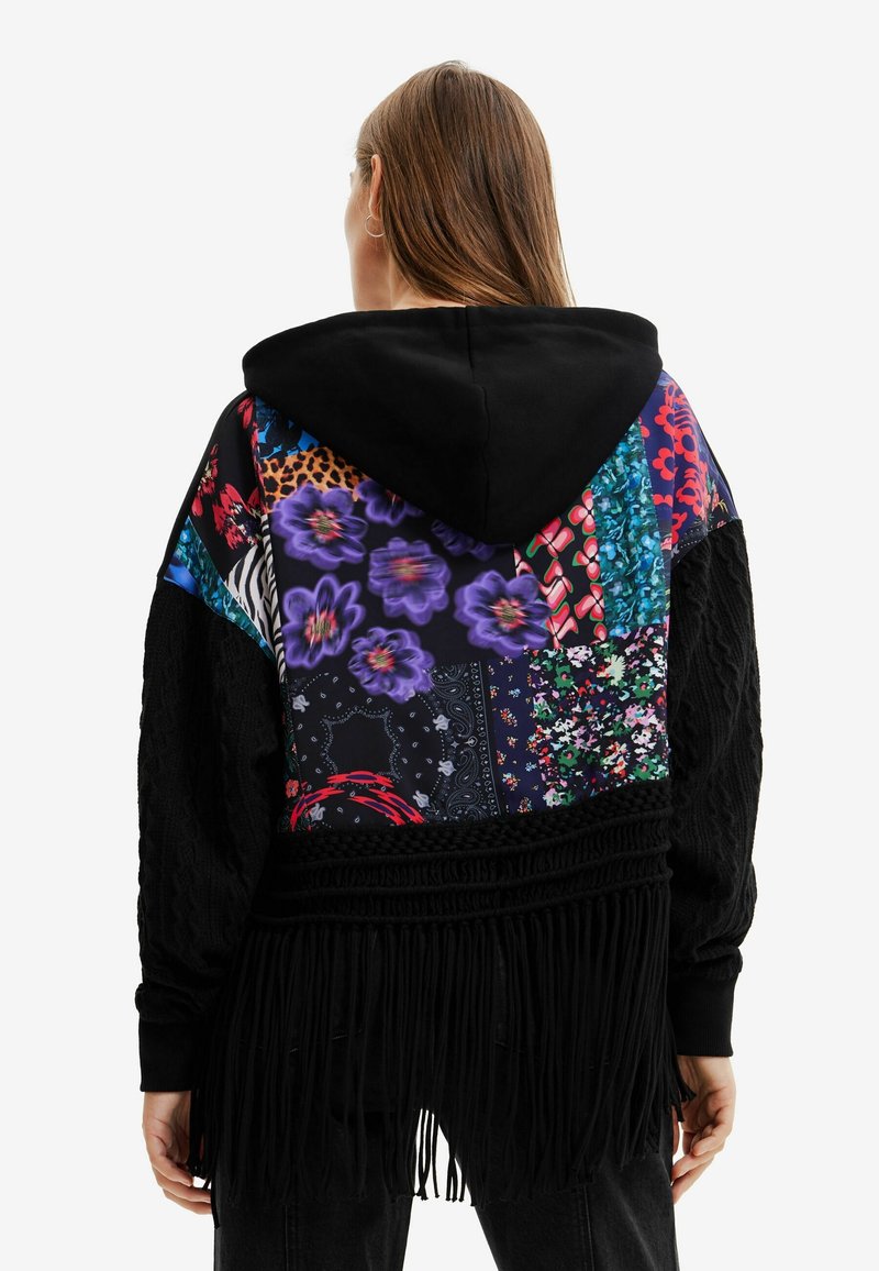 Sudadera con capucha que presenta un diseño de patchwork con patrones florales, estampados de animales y acentos de flecos. Fabricada en tejido negro con colores vibrantes.