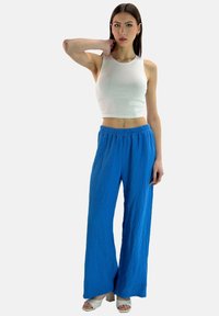 Top corto bianco con un design aderente abbinato a pantaloni blu larghi e strutturati. L'outfit presenta una vita alta e gambe larghe, con calzature leggere.