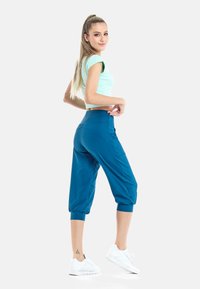 Top corto de color verde menta con mangas cortas, combinado con pantalones jogger sueltos en color azul azulado que se ajustan en los tobillos. Zapatillas deportivas blancas.