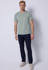 Světle zelené tričko s krátkým rukávem a výstřihem do V, v kombinaci s tmavě modrými džíny a světlými teniskami. Hladká textura, volný střih.