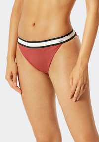 Červené bikiny s ribovanou texturou, které mají široký černobílý pruhovaný pas. Střih je nízký s minimálním pokrytím.