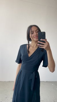 Vestido negro envolvente con mangas cortas en volante, escote en V y cintura atada. Tejido suave con una silueta fluida.