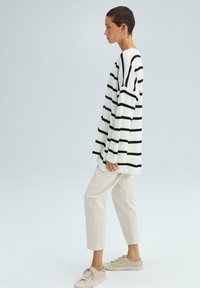 Pull en tricot oversize blanc avec des rayures noires, associé à un pantalon beige clair et des baskets beiges. Design simple et décontracté.