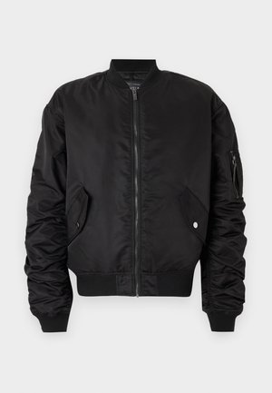 Juodas bomber stilius striukė su užtrauktuku priekyje, raštuotu apykaklės ir rankogalių dizainu, dviem šoninėm kišenėm ir naudingąja kišene kairiajame rankove.