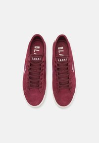 Μαρόνο σουέτ αθλητικά παπούτσια με λευκή σόλα, με υφασμάτινες και υφασματοποιημένες λεπτομέρειες και κορδόνια. Διαθέτουν το λογότυπο "LAKAI" στην γλώσσα και στο πλάι.