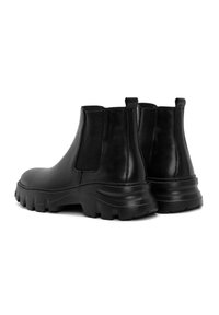 Botas Chelsea de cuero negro con una suela robusta y texturizada, paneles laterales elásticos y tiradores en la parte posterior para facilitar su colocación.