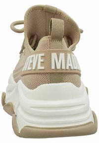 Béžové tenisky s síťovinovým svrškem, bílou robustní podrážkou a výrazným logem "STEVE MADDEN" na zadní straně. Obsahují poutko pro snadné obutí.